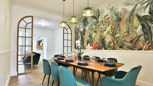 A dining area with a wooden table set for six, teal chairs, and a large tropical mural on the wall. - Villa Babil - Four Bedroom House, Sleeps 8 (Les Sables d'Olonne)