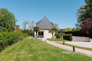 Un bâtiment doté d’un toit triangulaire, entouré d’une pelouse bien entretenue et d’arbres.
