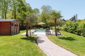 Eine Holzhütte mit Swimmingpool, umgeben von üppiger Vegetation und einem gepflasterten Weg.