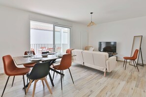 A modern living room with a dining table, sofa, TV, and a balcony view. - La Blancharderie - sur l'île de Noirmoutier (Barbâtre)