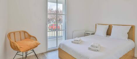 A bedroom with a bed, a chair, a window, and a view of the outside.