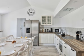 A modern kitchen with white cabinetry, a stainless steel refrigerator, a wooden countertop, and a clock on the wall. - Villa Sauvagère - Four Bedroom House, Sleeps 10 (Saint-Vincent-sur-Jard)