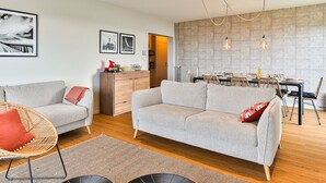 Een moderne woonkamer met een bank, een eethoek met tafel en stoelen, en een keuken op de achtergrond.