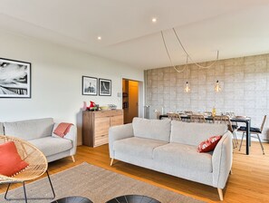 Un salon moderne avec un canapé, un coin repas comprenant une table et des chaises, et une cuisine en arrière-plan.