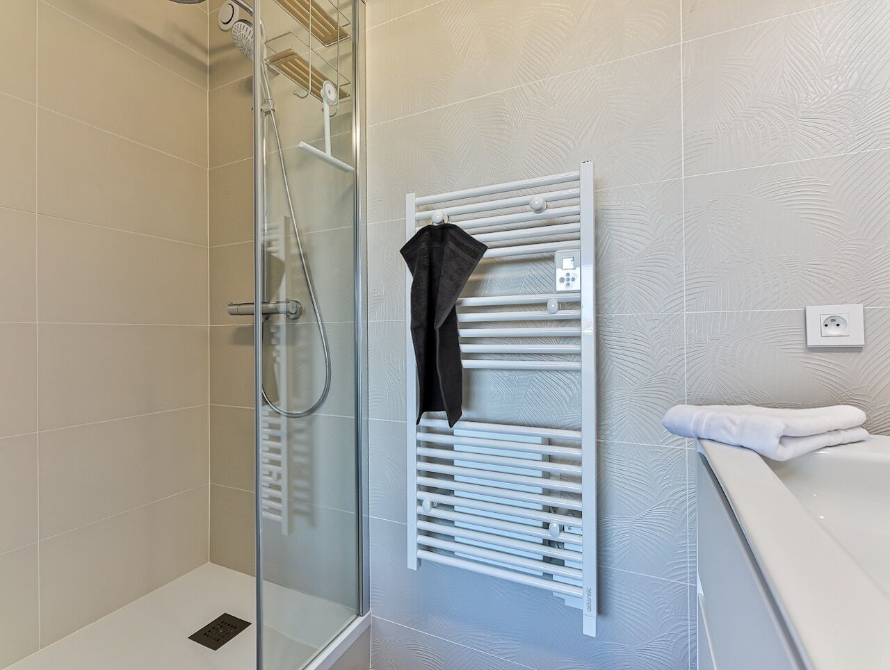 Een douche met een glazen deur, een witte handdoekhouder en een witte handdoek op het aanrecht.