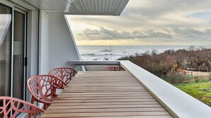 Een balkon met uitzicht op zee, houten vloeren en rode stoelen.