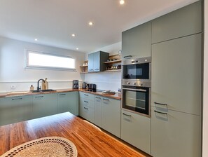Une cuisine moderne avec des meubles gris, un plan de travail en bois et des appareils électroménagers intégrés, notamment un four à micro-ondes et un four traditionnel.