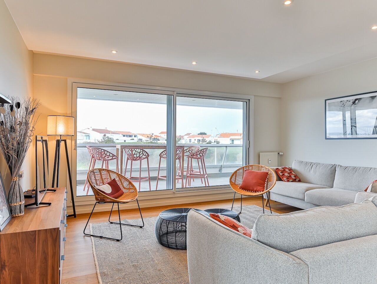 A modern living room with a sofa, two wicker chairs, a coffee table, and a large window with a view of buildings.