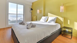 Een moderne slaapkamer met een groot bed, uitzicht op de oceaan, en een geel accentmuur.