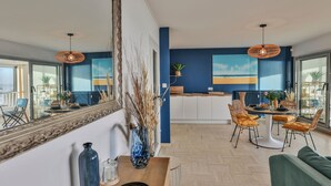 A modern living room with a dining area, large windows, and a view of the outdoors. - Les Loges du Remblai - vue imprenable sur la baie (Les Sables d'Olonne)