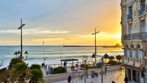 A coastal promenade with a sunset view, a pedestrian walkway, and a building with classical architecture. - Les Loges du Remblai - vue imprenable sur la baie (Les Sables d'Olonne)