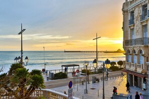 A coastal promenade with a sunset view, a pedestrian walkway, and a building with classical architecture. - Les Loges du Remblai - vue imprenable sur la baie (Les Sables d'Olonne)