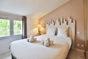 Ein Hotelzimmer mit einem großen Bett, einem Nachttisch mit Lampe und Blick auf Grünfläche.