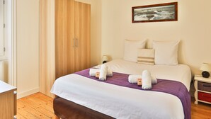 Quarto de hotel com cama, guarda-roupa, mesa de cabeceira, abajur e um quadro na parede.