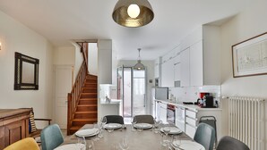 Uma sala de jantar com uma escada de madeira, uma cozinha com armários brancos e uma mesa de jantar posta para seis pessoas.
