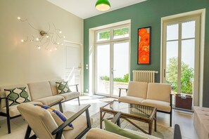A modern living room with a sofa, armchairs, a glass coffee table, and a unique wall light fixture. - La Maison des Lierres (Les Sables d'Olonne)