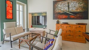 Uma sala de estar com sofá, poltronas, mesa de centro, televisão, um quadro e um aparador de madeira.