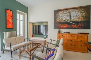 Ein Wohnzimmer mit einer Couch, Sesseln, einem Couchtisch, einem Fernseher, einem Gemälde und einem Holzschrank.