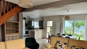 A modern living room with a sofa, a black chair, a dining table with chairs, a kitchen area, and a staircase. - Bright house with enclosed garden, near beaches Lézardrieux (Lézardrieux)