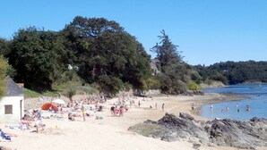 A beach with people sunbathing and swimming, surrounded by trees and a stone building. - Bright house with enclosed garden, near beaches Lézardrieux (Lézardrieux)