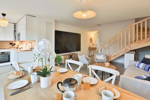 Eine moderne Küche mit weißen Schränken, ein Essbereich mit Holztisch und Stühlen sowie eine Treppe, die zu einem Erker führt.
