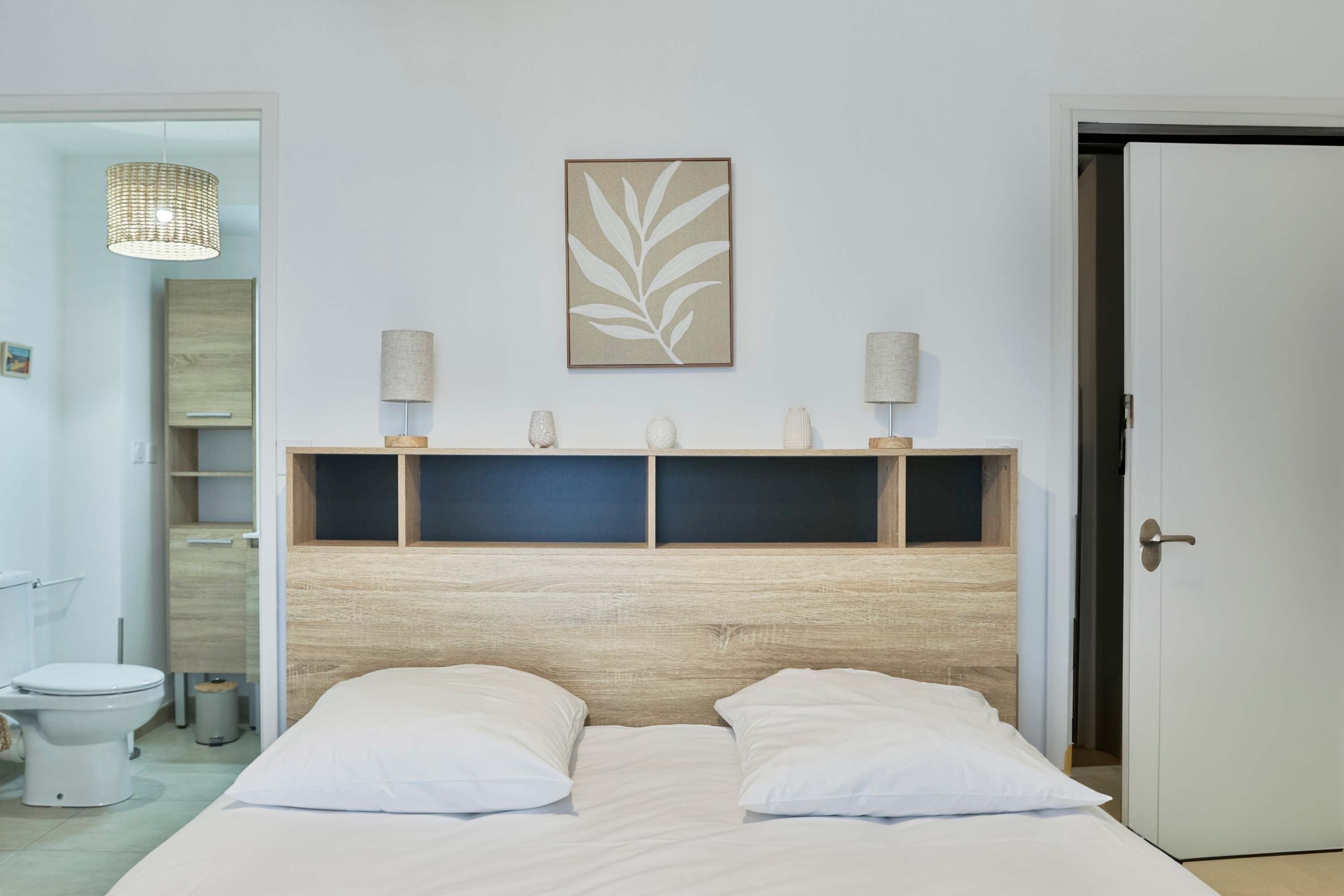A bedroom with a bed, a headboard, a wall-mounted artwork, bedside lamps, and a door.