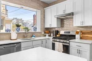 A modern kitchen with white cabinets, a large island, a stove, and a window with a view of the outside. - Beach Block Luxury | Sleeps 20 w/ Bar Room (Ventnor City)