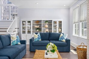 A living room with two dark blue sofas, a white coffee table, and a decorative vase with flowers. - Beach Block Luxury | Sleeps 20 w/ Bar Room (Ventnor City)