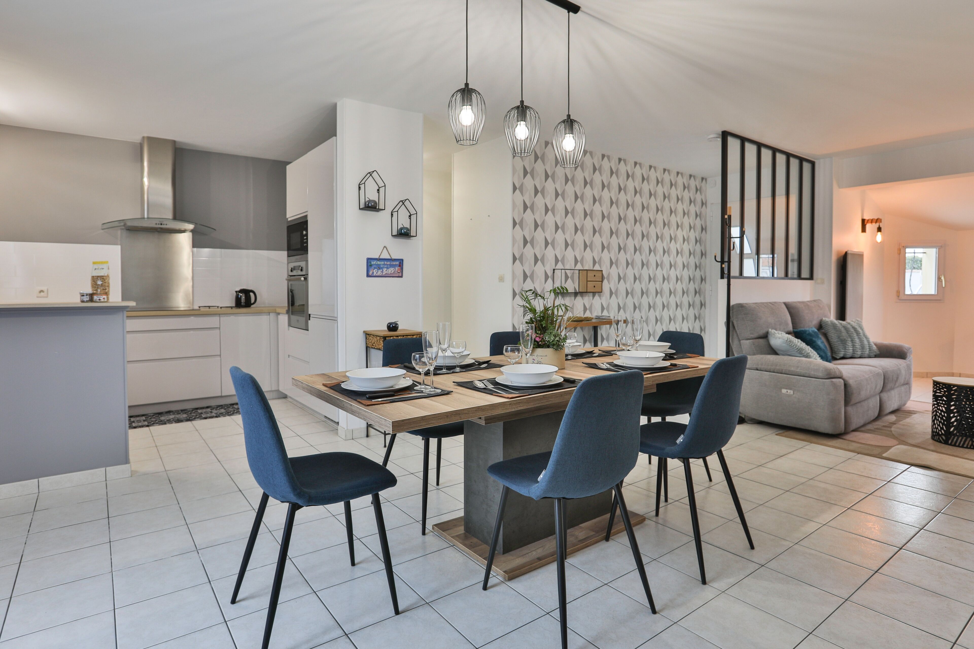 Een moderne keuken met een eetgedeelte, met een centraal eiland, hanglampen en een grijs patroon op de muur.