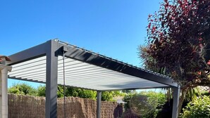 Uma banheira de hidromassagem sob uma pérgola em um quintal com deck de madeira e cerca.
