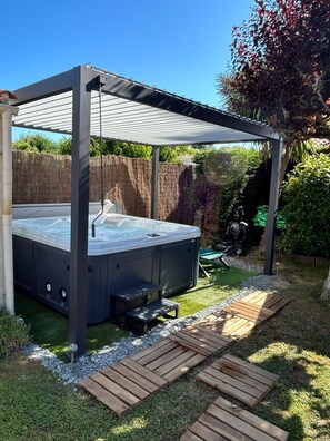 Ein Whirlpool unter einer Pergola in einem Garten mit einer Holzterrasse und einem Zaun.