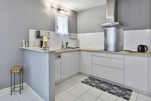 Eine moderne Küche mit weißen Schränken, einer Edelstahl-Dunstabzugshaube und einer kleinen Kochinsel mit Spüle.