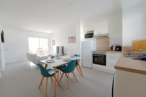 A modern kitchen with white cabinets, a microwave, and a stove. There is a dining area with a table and chairs.