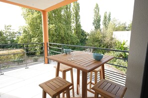 A wooden table and chairs on a balcony with a railing, a view of trees and a building in the background. - Clos des Sables B13 - Two Bedroom Apartment, Sleeps 4 (Les Herbiers)