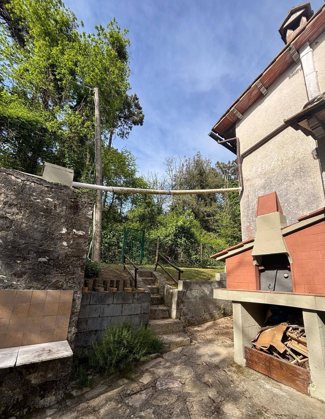 Una scala in pietra conduce a un edificio in mattoni con un camino, immerso nel verde.