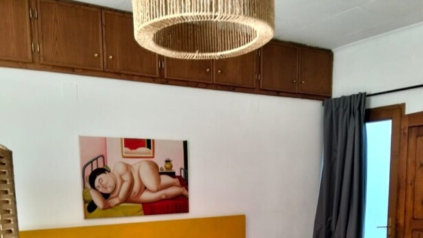 A bedroom with a bed, a painting on the wall, a wooden headboard, and a window with curtains. - Studio Apartment - Corner 28 (Bolsena)