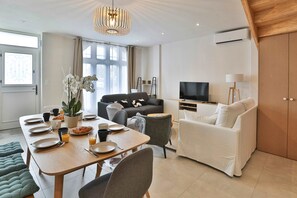 Una sala de estar moderna con comedor, sofá, televisor y un ventanal grande.