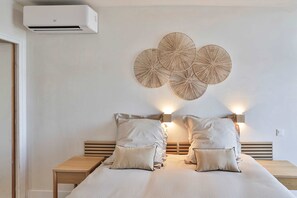 Un dormitorio con cama, mesitas de noche, aire acondicionado de pared y decoración mural.