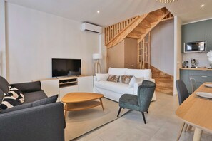 Una sala de estar moderna con televisor, sofá, mesa de centro y una escalera que lleva a una cocina.