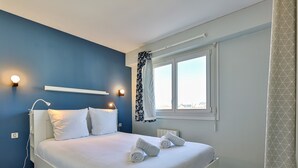 Ein Schlafzimmer mit Bett, Nachttischlampen, einem Fenster mit Vorhängen und Blick nach draußen.