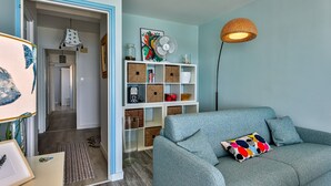 Ein Zimmer mit einem blauen Sofa, einem Bücherregal, einer Stehlampe und einer Tür zu einem anderen Raum.
