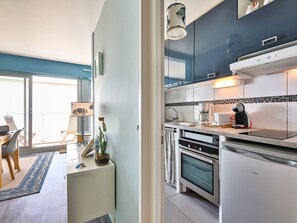 A modern kitchen with a coffee maker, oven, and a dining area with chairs and a table. - Reflets d'Océan - vue imprenable sur la mer (Les Sables d'Olonne)