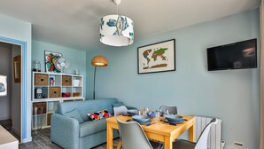 Ein modernes Wohnzimmer mit einer Couch, einem Esstisch, Stühlen, einem Fernseher, einer Weltkarte und einem Bücherregal.