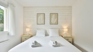 Habitación de hotel con cama, dos mesitas de noche, dos lámparas de pared, dos almohadas, dos toallas dobladas y dos obras de arte con hojas enmarcadas en la pared.
