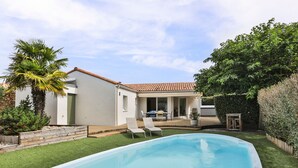 Una piscina con zona de patio, un edificio blanco y una puerta verde.