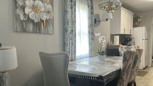Ein Essbereich mit Tisch, Stühlen, einer Chandelüster und einer Küche im Hintergrund.