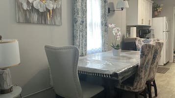 Un espace repas comprenant une table, des chaises, un lustre et une cuisine en arrière-plan.