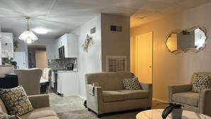 Ein Wohnzimmer mit einer Couch, Sesseln, einem Couchtisch und einer Küche im Hintergrund.