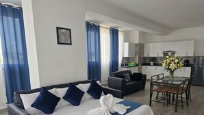 A modern hotel room with a bed, a sofa, a dining table, and a kitchen area. - Ducassi Penthouses Rooft Pool (Punta Cana)