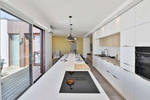 A modern kitchen with a central island, built-in appliances, and a dining area with a long table. - Villa Moovéa - Four Bedroom House, Sleeps 8 (Les Sables d'Olonne)